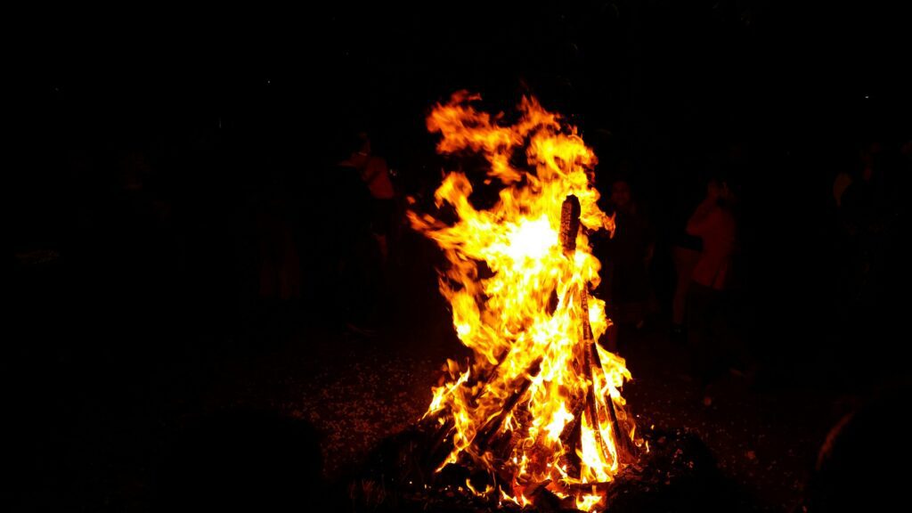 Bonfire flames during Holika Dahan reflected on a phone screen as people gather around.