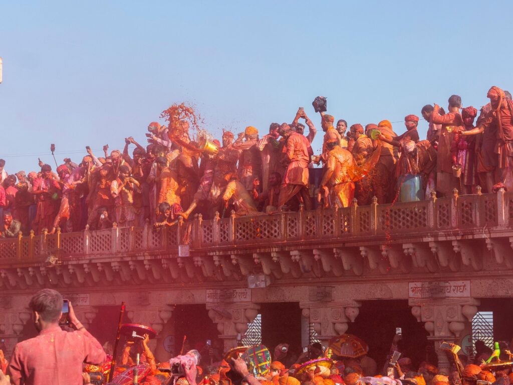 Crowd Holi festival in jaipur on a temple balcony, throwing vibrant colored powder into the air.
