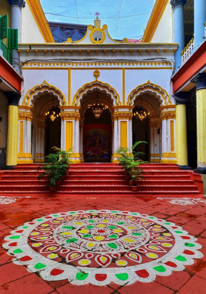 Colorful traditional rangoli design in front of a house entrance with red steps and decorative plants