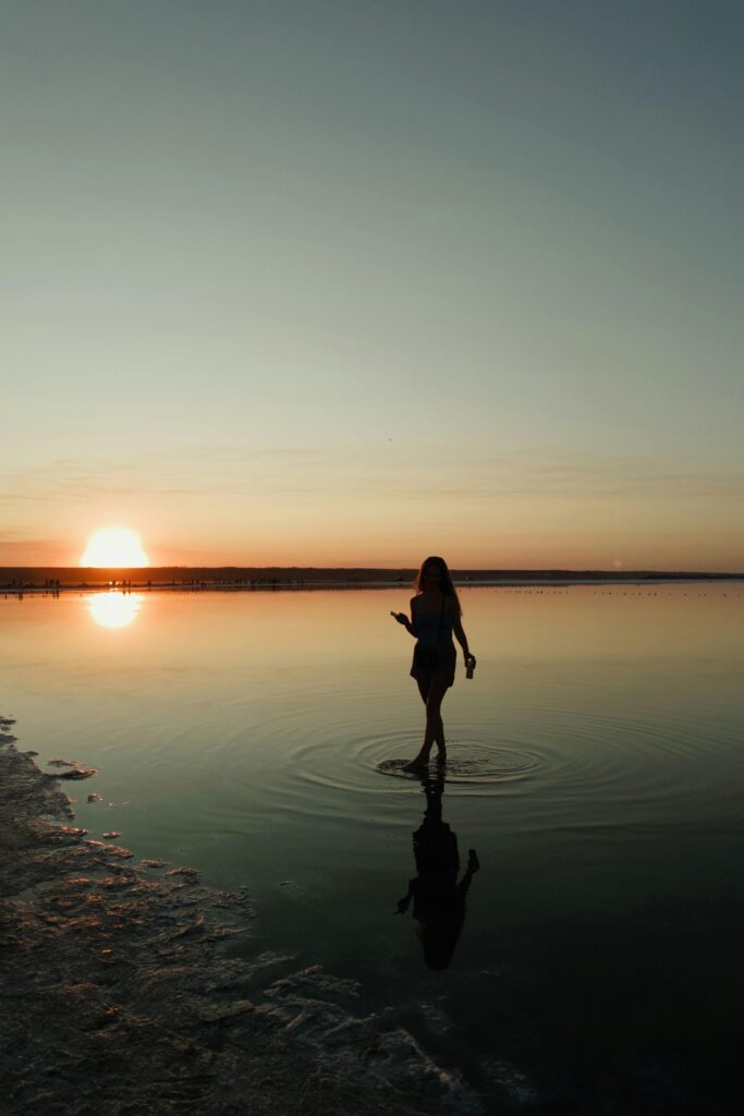 A lone figure creates ripples in the tranquil waters of an Odessa lake at sunset, enveloped in natural beauty.